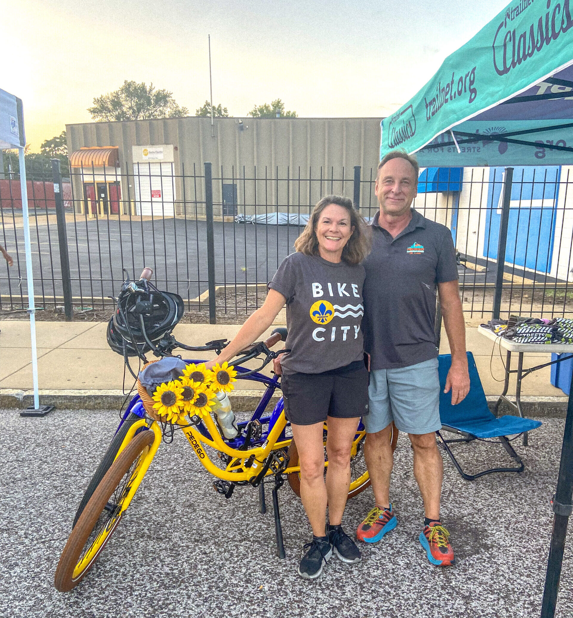 Bill and Carla Sauerwein stand next to a Pedego Electric Bike beside a Trailnet pop-up tent.