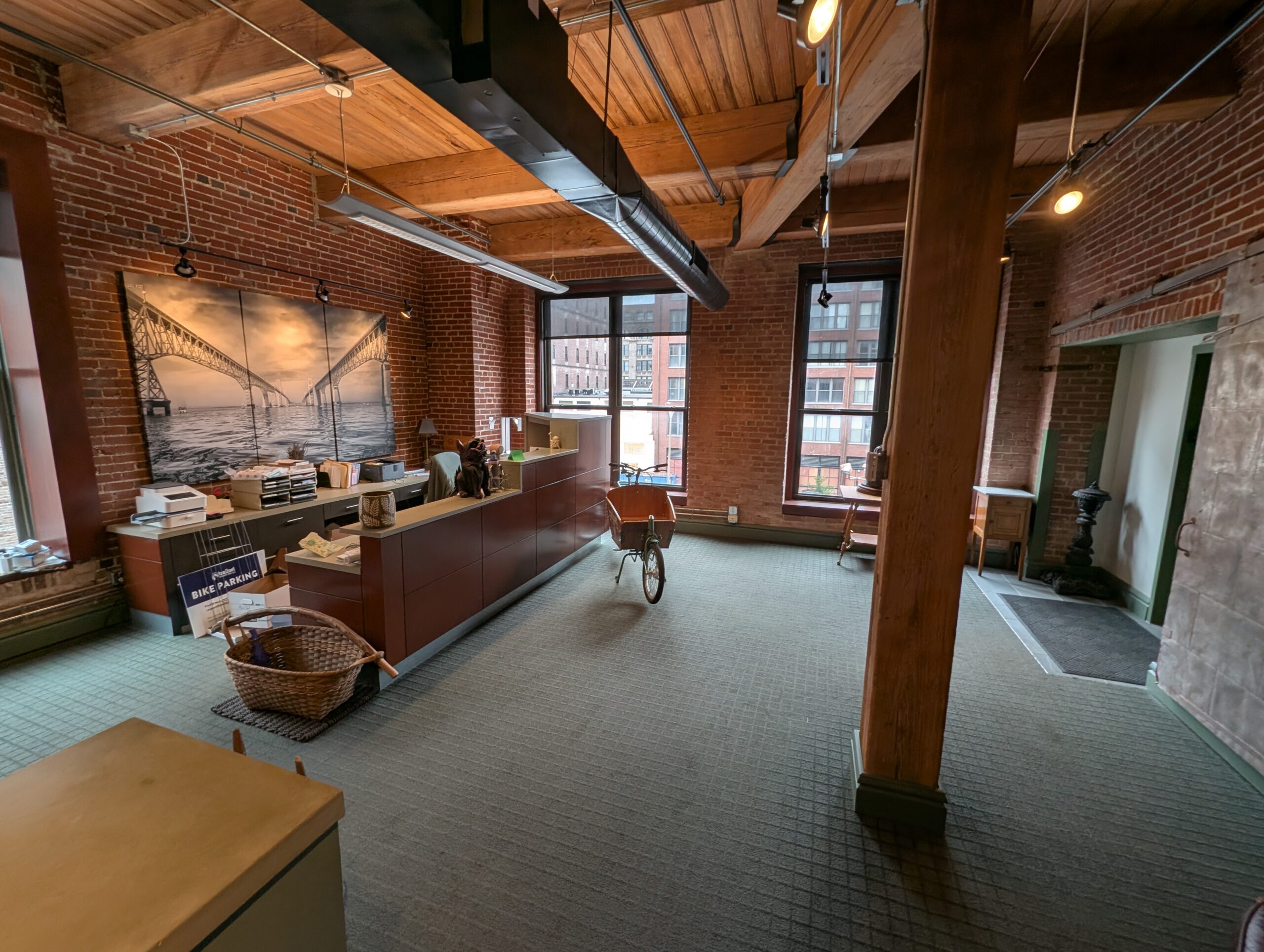 An office area, with a large counter on the left, tall windows, and a large wooden beam toward the right of the room.