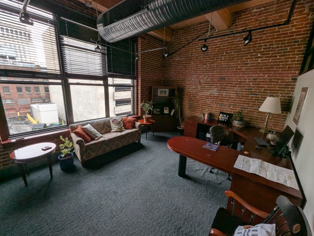An office with a couch in front of large windows, and a desk and chair. 